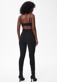 Czarne legginsy z wysokim stanem o gładkiej fakturze, zestawione z czarnym, krótkim topem na ramiączkach. Modelka nosi czarne botki na obcasie.