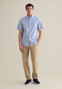 Camisa de botones de manga corta con rayas verticales azules y blancas, combinada con chinos color beige y zapatillas negras. Textura de tela suave.