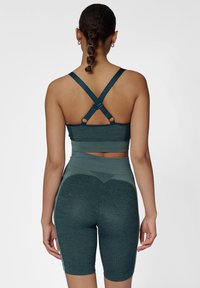 Szmaragdowy stanik sportowy z krzyżującymi się ramiączkami i siateczkowymi detalami, w połączeniu z dopasowanymi, wysokim stanem szortami rowerowymi z fakturowanym pasem.
