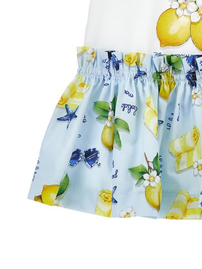 Φούστα ανοιχτού μπλε με εκτυπώσεις λεμονιού, λουλουδιών, αστερία και ριγέ γλυκίσματα, με ζωνάρι στη μέση, συνδυασμένη με λευκό τοπ που έχει γραφικά λεμονιού.