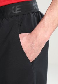 Schwarze Sportshorts mit einem strukturierten Bund, auf dem das "NIKE"-Logo prangt, seitlichen Taschen und einem lockeren Schnitt für Komfort.
