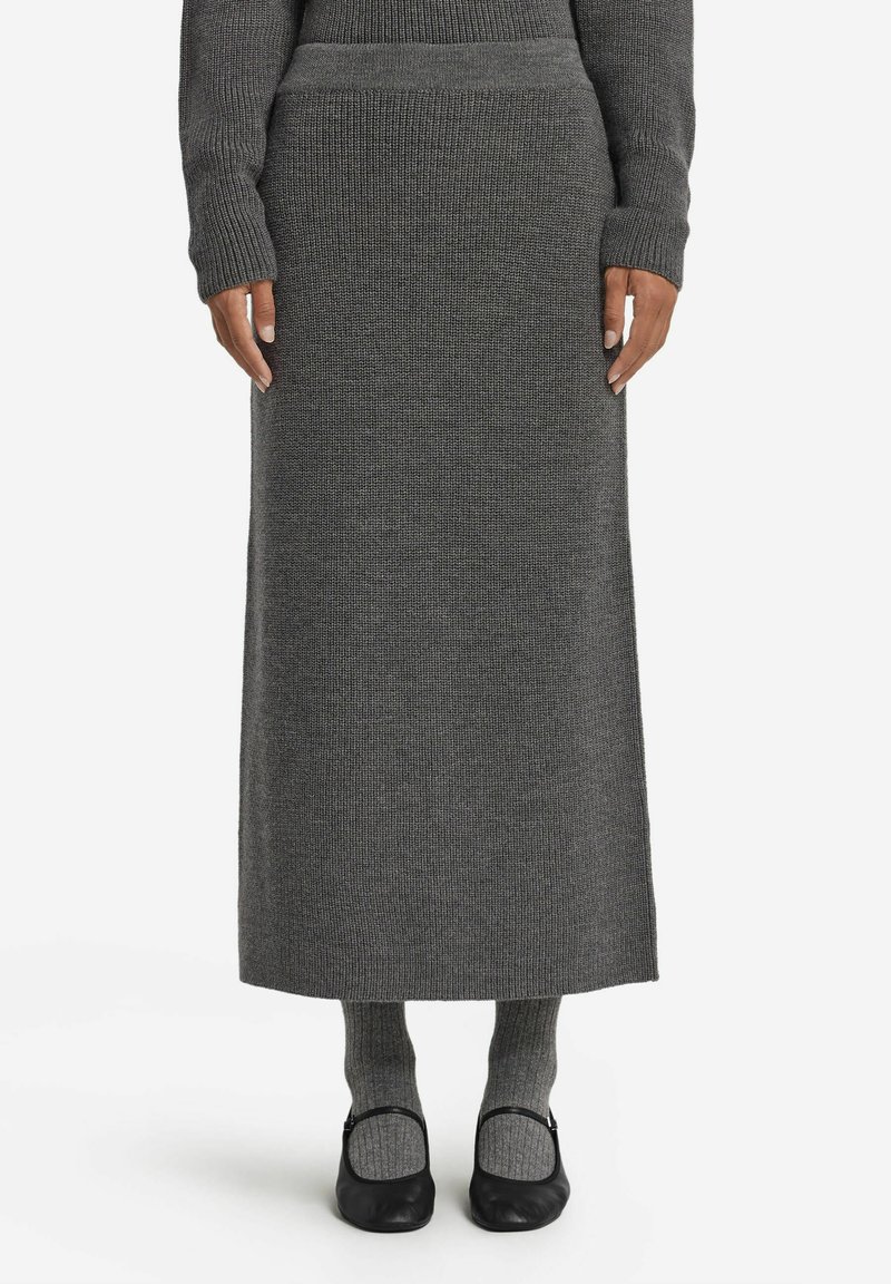 Grå stickad maxibig med en ribbad struktur, kombinerad med grå knäkorta strumpor och svarta ballerinas. Enkel, rak silhuett framhäver längden.