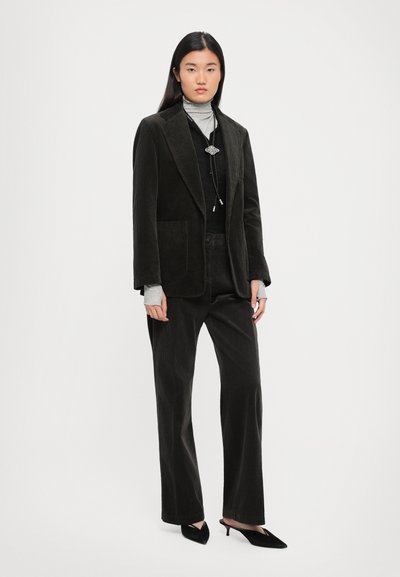 Black corduroy blazer with notch lapels, gray turtleneck, and matching pants. Model wears pointed black heels. Textured fabric visible.