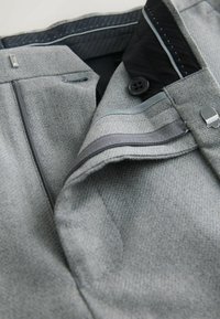 Grijze aansluitende broek met een gestructureerde stof. Voorzien van een zwarte tailleband, knoopsluiting en contrasterende rits. Accenten zijn subtiele grijze biezen.