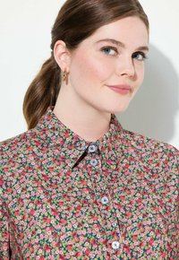 Camicia a bottoni floreale con un pattern colorato di fiori rosa e rossi su uno sfondo blu, con colletto e bottoni blu.