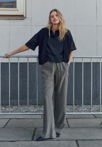 Camicia nera a maniche corte con bottoni sotto un gilet in maglia nera texturizzata. Pantaloni grigi larghi con tasche laterali. Tessuto morbido e design semplice.