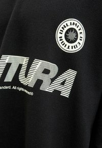 A fekete textúrájú anyagon kiemelkedő fehér "VENTURA" felirat és egy kör alakú badge található, rajta az "UNLIMITED EDITION" felirattal és egy nap szimbólummal.