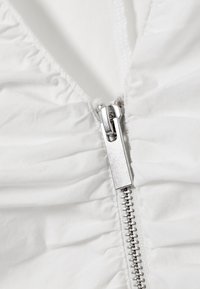 Κοντινό πλάνο ασημένιου μεταλλικού φερμουάρ σε λευκό ρουχισμό με συγκεντρωμένο ύφασμα, με εμφανή δόντια φερμουάρ και λεπτομέρειες ραφής.