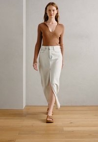 Haut à manches longues côtelé marron associé à une jupe en denim blanche taille haute, longueur sol, avec une fente à l'avant. Sandales à plateforme marron.