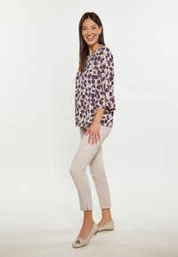 Blusa leggera color crema con motivo a foglie viola, maniche a tre quarti; abbinata a pantaloni tapered beige chiaro e ballerine beige.