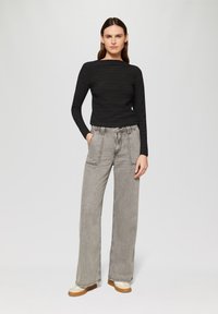 Haut noir à rayures et à manches longues associé à un pantalon large gris clair avec double poches avant et couture contrastante.