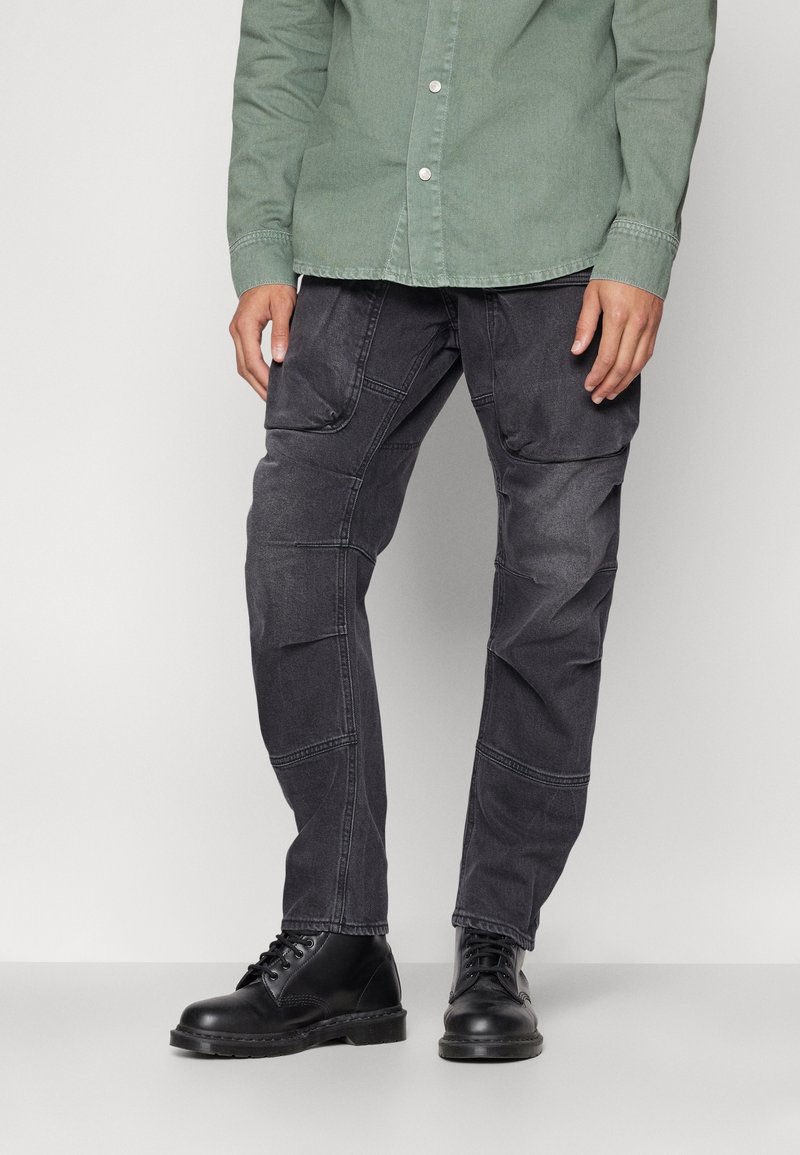 Svarta, strukturerade cargobyxor med flera fickor och en smal passform, parat med svarta snörstövlar och en grön skjorta med knappar.