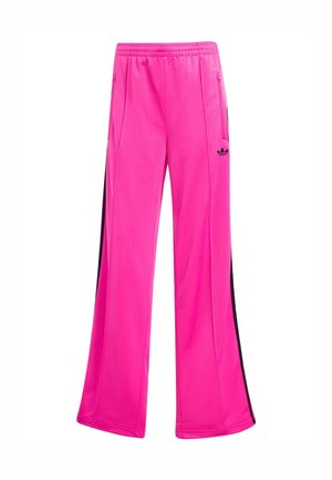 Pantalons de jogging en polyester rose avec une coupe large, présentant des rayures noires sur les côtés et un logo Adidas sur la jambe gauche.