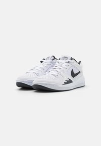 Bílé sportovní tenisky s texturovaným koženým svrškem, černým logem Nike a šněrovacím designem. Obsahují polstrovaný límec a gumovou podrážku.