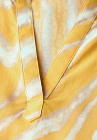 Tessuto giallo con un motivo a onde in tonalità più chiare, caratterizzato da un design a scollo a V e dettagli di cucitura a contrasto. Tecnologia liscia.