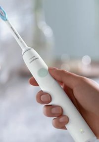 Spazzolino elettrico con corpo bianco, setole blu e pulsante di accensione verde chiaro. Forma arrotondata con un design elegante, accenti minimi.