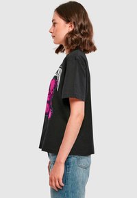 Sort bomulds t-shirt med korte ærmer, der har et markant pink grafisk design på forsiden. Standard pasform, rund halsudskæring og blød tekstur.