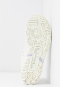 Vit sneakersula med texturerad gummi, cirkulärt greppmönster och ljusrosa accenter. Har en torsionsstång för stöd och stabilitet.