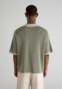 Green short-sleeve sweater with textured knit pattern, cream ribbed collar and hem, featuring a relaxed fit and straight cut.