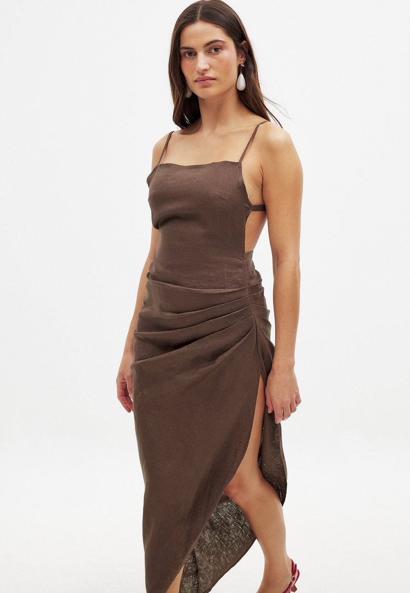 Ruskea pellavamekko, jossa on ohuet hihnat, kappaleenmyötäinen leikkaus, kippurainen hame, korkea halkio, teksturoitu kangas, yhdistettynä valkoisiin pisaramuotoisiin korvakoruihin.