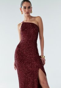 Burgundy sequin evening dress with a fitted silhouette, one-shoulder design, thigh-high slit, and a smooth, textured finish.