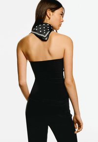 Schwarzes trägerloses Top mit taillierter Passform, kombiniert mit einem schwarz-weißen gepunkteten Schal, der hinten gebunden ist. Schlichtes und elegantes Erscheinungsbild.