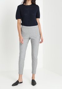 Pull en maille marine à manches courtes, associé à un pantalon tailleur gris clair. Le mannequin porte des mules noires à enfiler. Esthétique minimaliste.