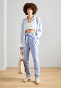 Lyseblå bukser med sløyfedetalj i midjen, kombinert med en hvit cropped topp og stripete skjorte med knapper. Beige sneakers og tote bag.