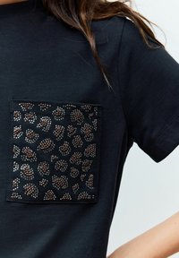 T-shirt nero a maniche corte con una grande tasca caratterizzata da un design in stampa leopardata argento e bronzo realizzato in strass.