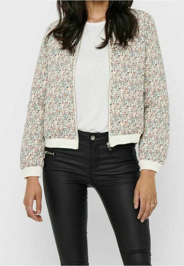 Veste bomber fleurie crème avec motifs orange et verts, poignets côtelés et fermeture éclair avant. Associée à un jean skinny noir.