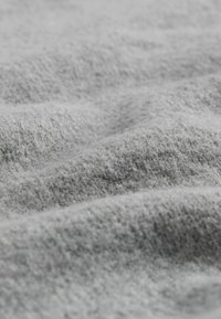 Sivo blago z mehko, teksturirano površino, ki prikazuje nežne valove in puhast videz, ustvarja prijeten in topel vizual.