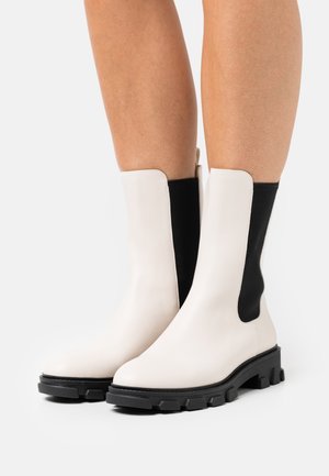 Bottes blanches en cuir à cheville avec des panneaux latéraux élastiques noirs, bouts arrondis et semelles épaisses en caoutchouc noir. Texture lisse et design élégant.