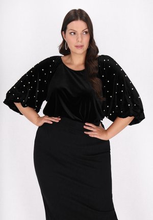 Zwarte fluwelen top met parelaccenten, voorzien van pofmouwen. Draagt met een strak zwarte rok. Glad textuur, elegante stijl.