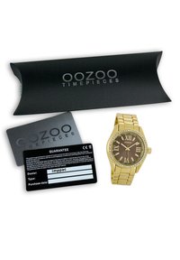 Montre-bracelet en or avec un boîtier rectangulaire, un cadran marron, des chiffres romains, des accents en cristal et un bracelet en métal doré, accompagnée d'une carte de garantie et d'une boîte.