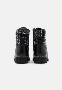 Botas de cuero negras hasta el tobillo con un cuello de punto texturizado en blanco y negro, tacón bajo y detalle de costura blanca en la suela.