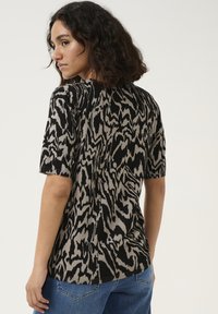 Striktop med et sort og beige abstrakt mønster, korte ærmer og en afslappet pasform. Stoffet har en blød tekstur med ribbede detaljer.