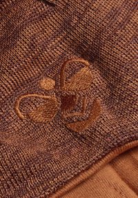 Tela texturizada marrón con un diseño bordado de abeja en un marrón ligeramente más oscuro. La tela parece tejida y suave, con un bordado detallado.