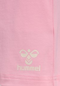 Różowy materiał sportowy o gładkiej fakturze z wyróżniającym się białym logo Hummel oraz stylizowanym wzorem pszczoły w pobliżu dołu.