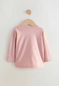Roze T-shirt met lange mouwen aan een houten hanger; eenvoudig ontwerp, zachte textuur, ronde halslijn, afgewerkte randen, zonder zichtbare patronen of grafische elementen.