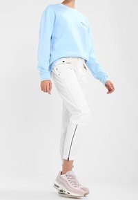Felpa azzurro chiaro con collo a giro, pantaloni cargo bianchi con zip e sneakers rosa con dettagli in rete e suole in gomma.