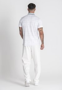 Biele polokošeľové tričko s krátkym rukávom a jemným vzorom, doplnené kontrastným golierom. V páre s štruktúrovanými bielymi nohavicami a bielymi teniskami.