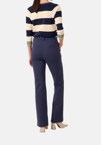 Kvinna klädd i marinblå åtsittande byxor, beige blockklackar och en långärmad tröja med breda marinblå och krämfärgade horisontella ränder.