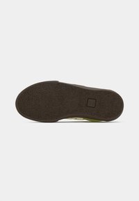 Sola de sapato com uma superfície de borracha texturizada castanha, apresentando uma forma arredondada e um pequeno logótipo no centro, realçada com uma borda verde.