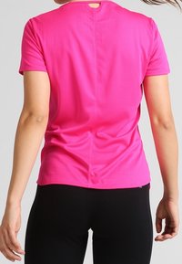 Camiseta ajustada de manga corta en tejido rosa brillante, con escote redondo y una pequeña abertura en la espalda, de textura suave y elástica.