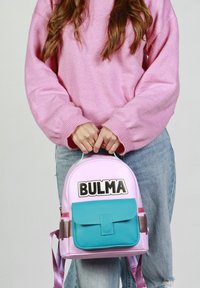 Sac à dos à forme arrondie, fabriqué en matériaux violet et turquoise ; doté d'une poche frontale à rabat et de l'étiquette « BULMA » en gras.