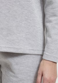Vaaleanharmaa puuvillainen vapaa-ajan asukokonaisuus, jossa on teksturoitu, pehmeä pinta. T-paidassa on pitkät hihat ja suora helma, kun taas housut ovat istuvat.