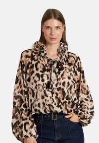 Blusa de estampado de leopardo con un cuello con volantes, mangas largas y tela ligera; presenta un lazo en el cuello y una superficie texturizada.