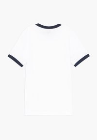Camiseta blanca de manga corta con ribete en azul marino en el cuello y los puños, colocada plana mostrando el lado posterior.