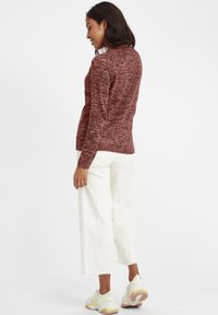 Maroon textured long-sleeve sweater, paired with white wide-leg pants and white sneakers with yellow accents. Rear view of outfit.