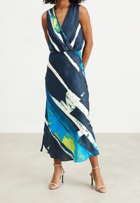 Bezramenné zavinovací šaty z tmavě námořnické látky s abstraktními modrými, bílými a zelenými štětcovými tahy. Délka sahá do poloviny lýtek.